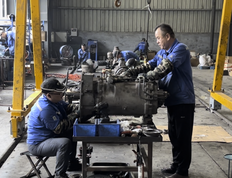 Teknikistoj laborantaj kun motorkomponentoj en la fabriko